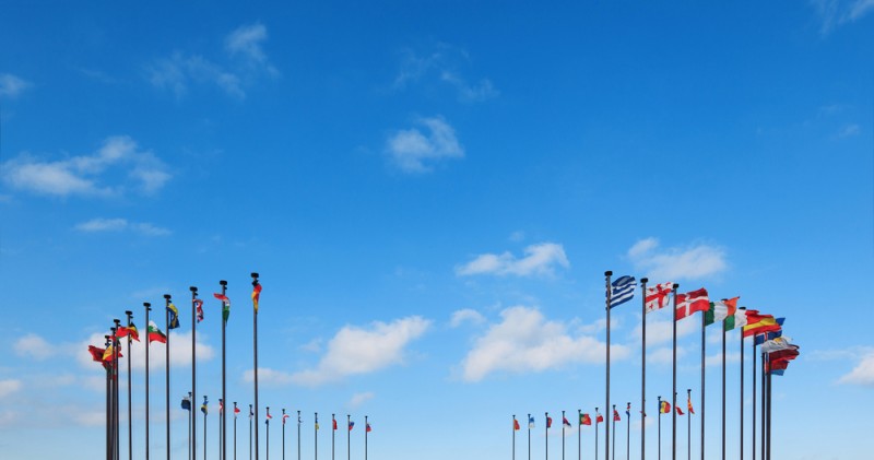 Flags of different countries on a flagpole against a blue sky
